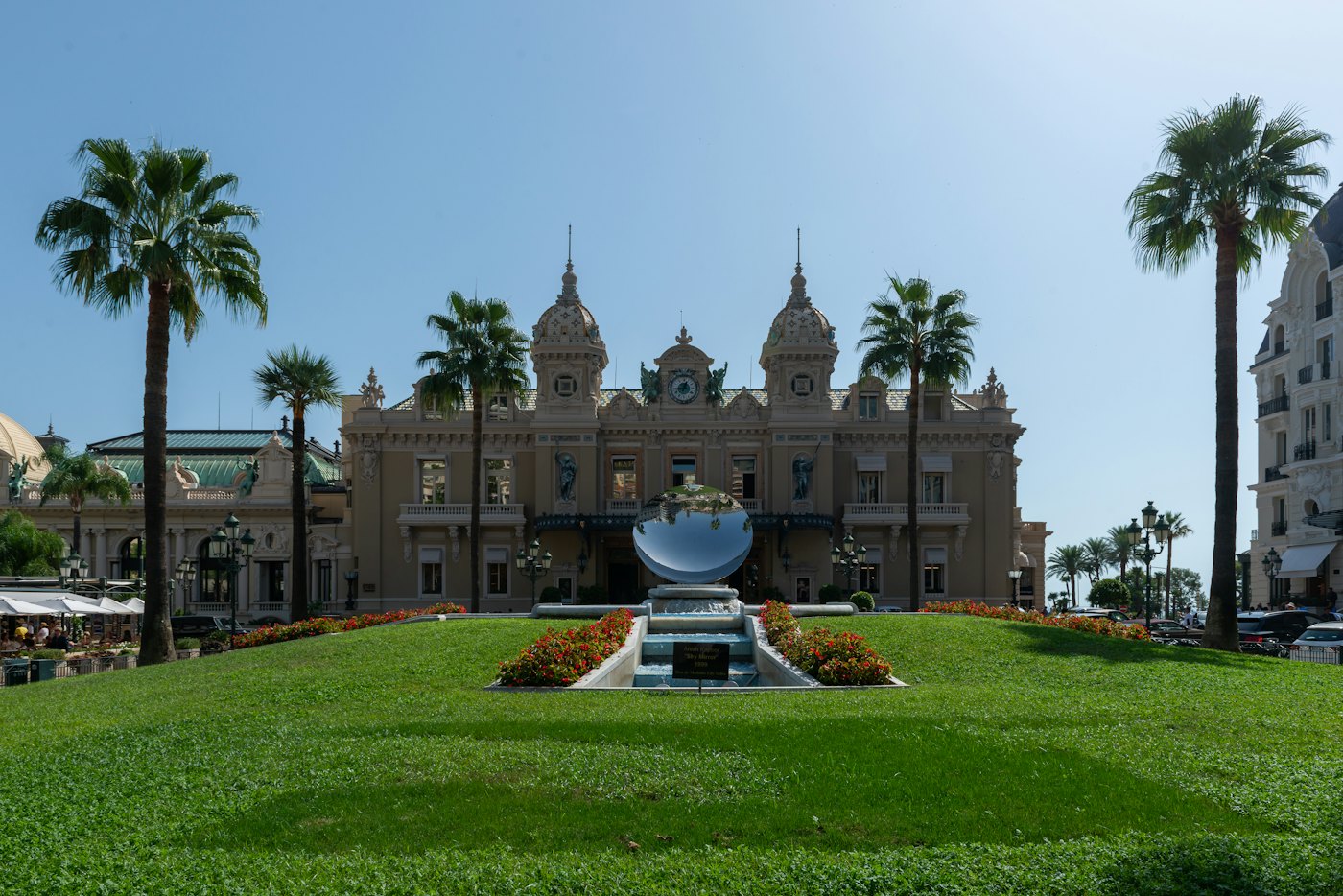 La place du Casino de Monte-Carlo, ses palmiers et sa sculpture miroir, avec les terrasses de café