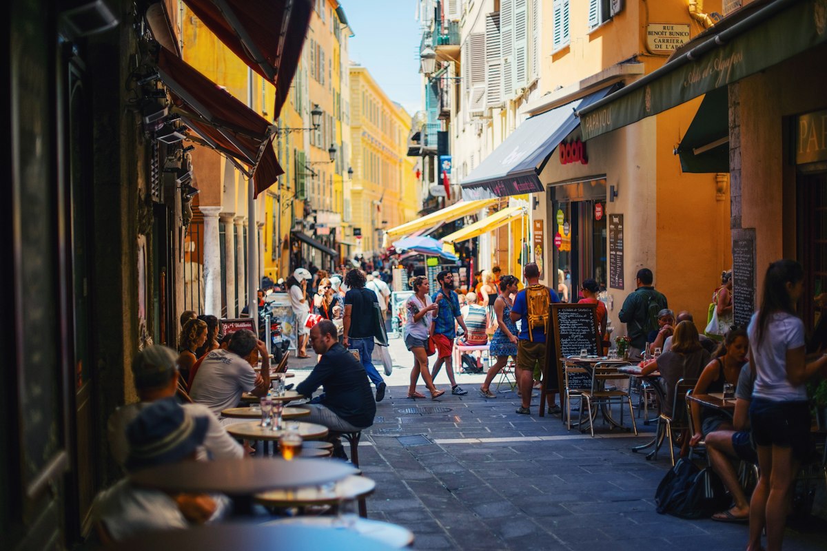 Terrasses et passants dans une ruelle ocre du centre ancien de Nice