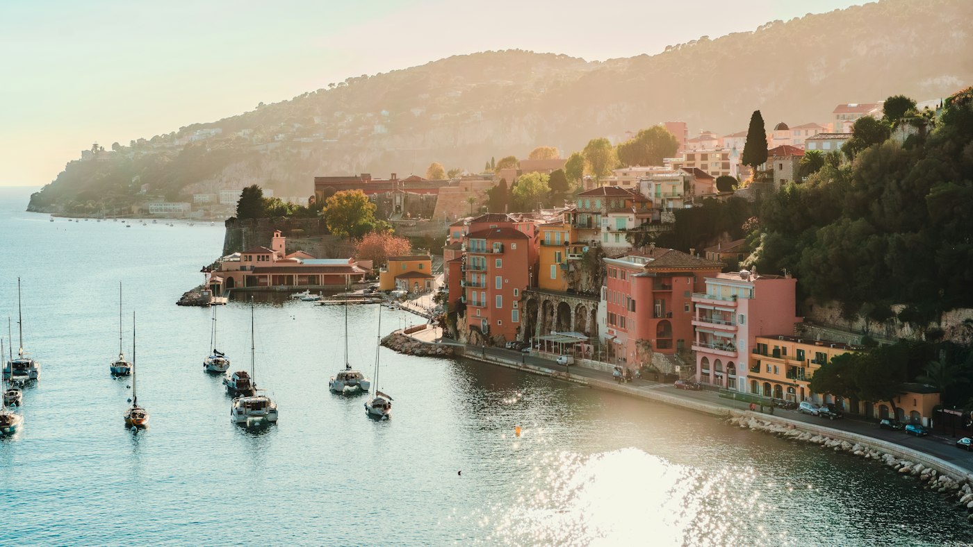 Les façades roses et ocre de Villefranche-sur-Mer au bord de l'eau, avec des voiliers dans la rade