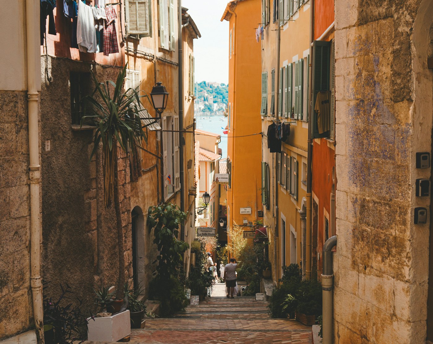Un escalier pavé entre des façades ocre, avec la mer au bout de la ruelle, dans la vieille ville de Villefranche-sur-Mer